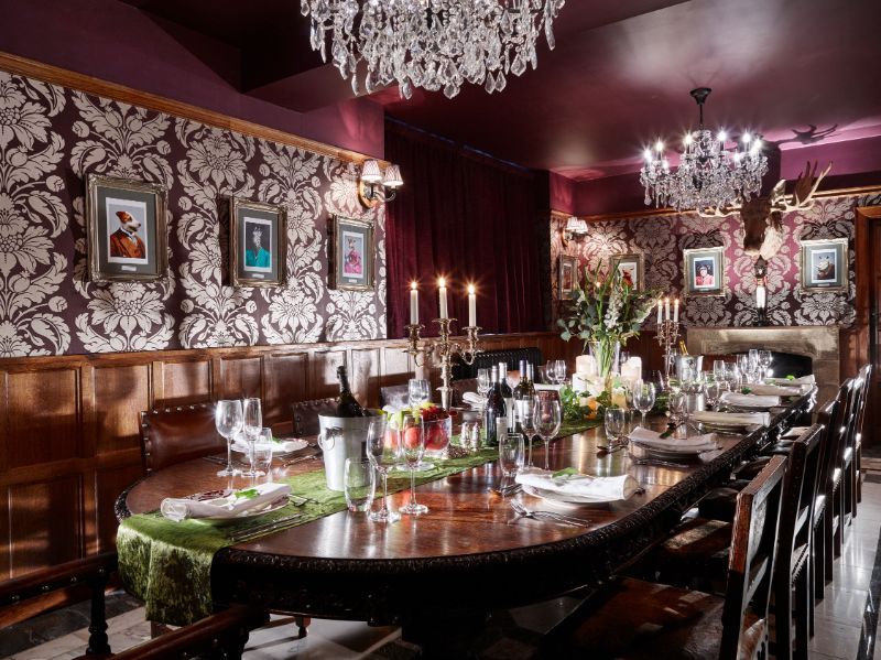 Elegant dark wood dining room with crystal chandeliers, candlelit table, and floral centerpiece