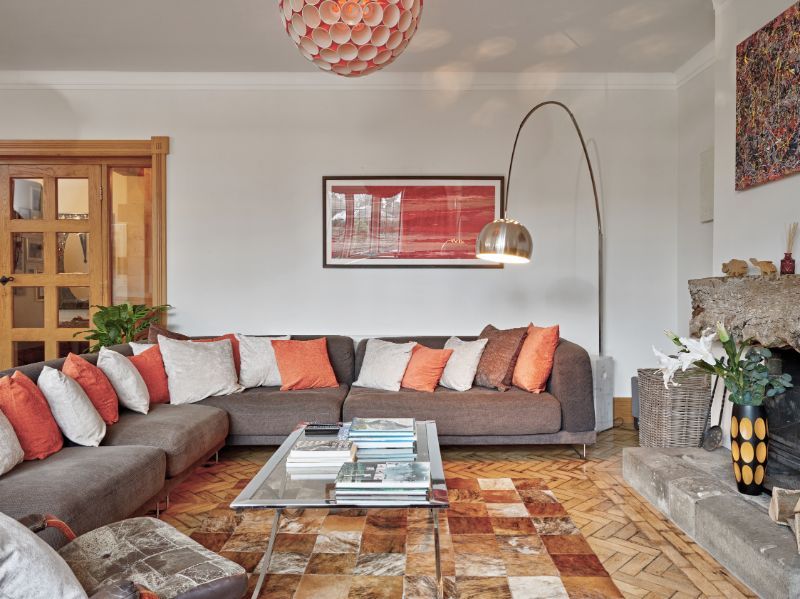 Modern living room with gray sectional, orange pillows, coffee table, arc floor lamp, and patterned rug