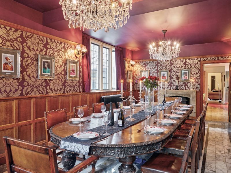 Elegant dining room with a long set table, chandeliers, red walls, and ornate decor