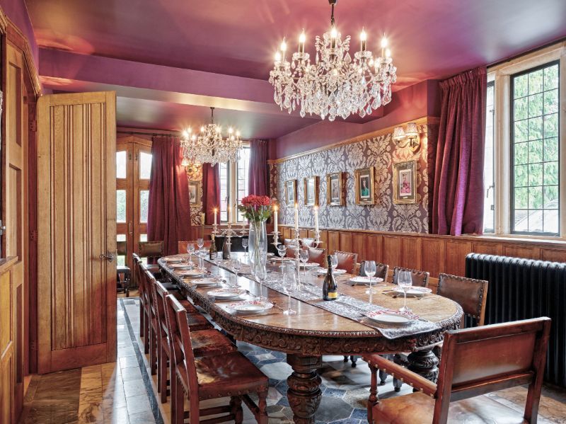 Elegant dining room with chandelier, long wooden table, red walls, and large windows