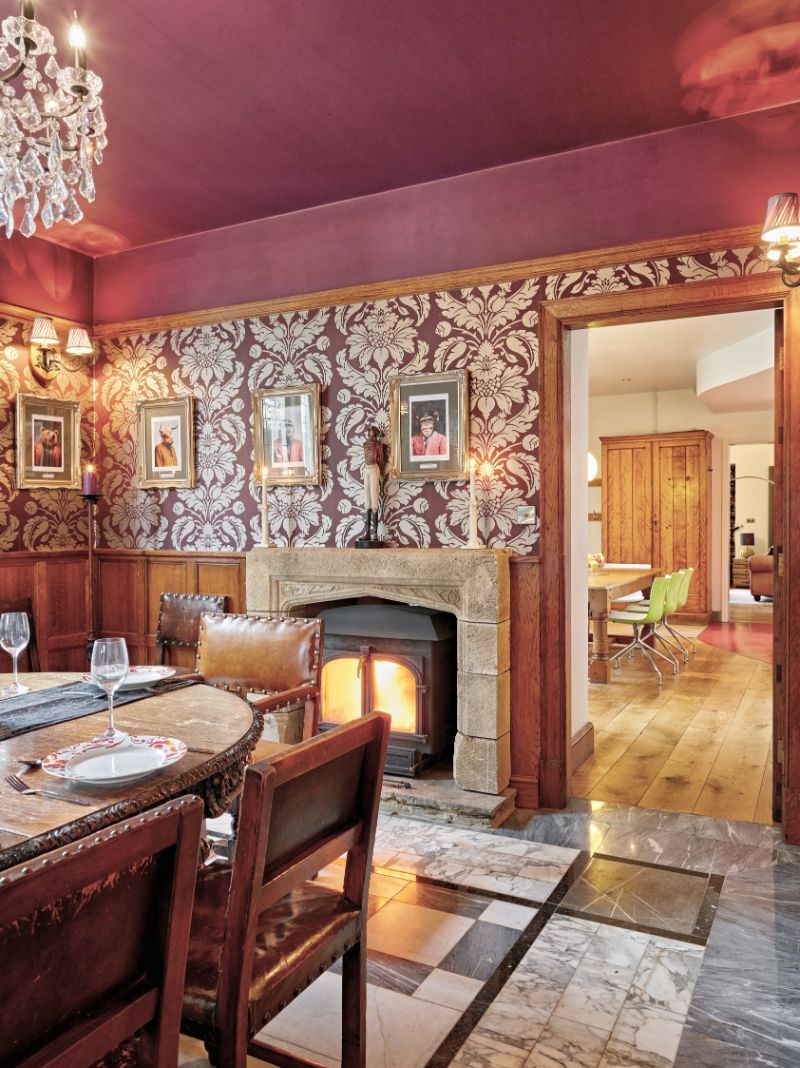 Cozy wood-paneled dining room with a lit fireplace, chandelier, and patterned wallpaper