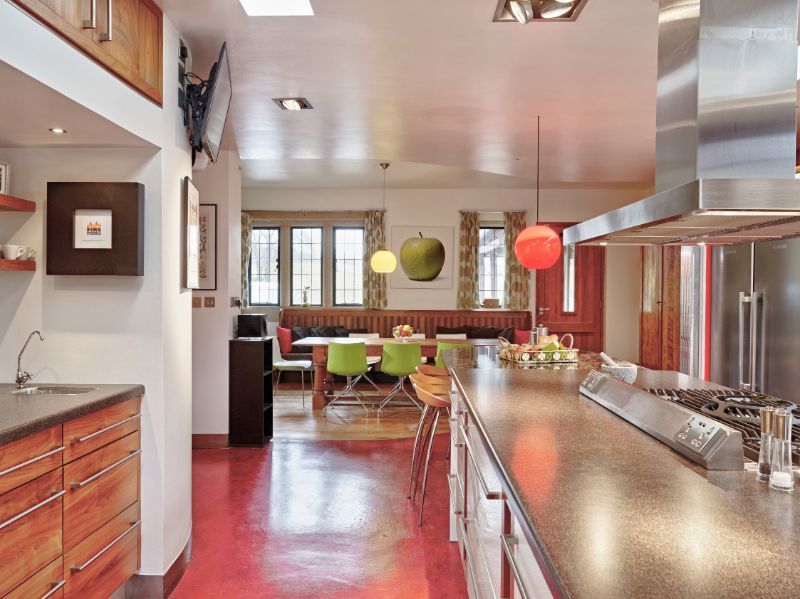 Modern kitchen with stainless steel island, red floor, and green dining chairs by large windows