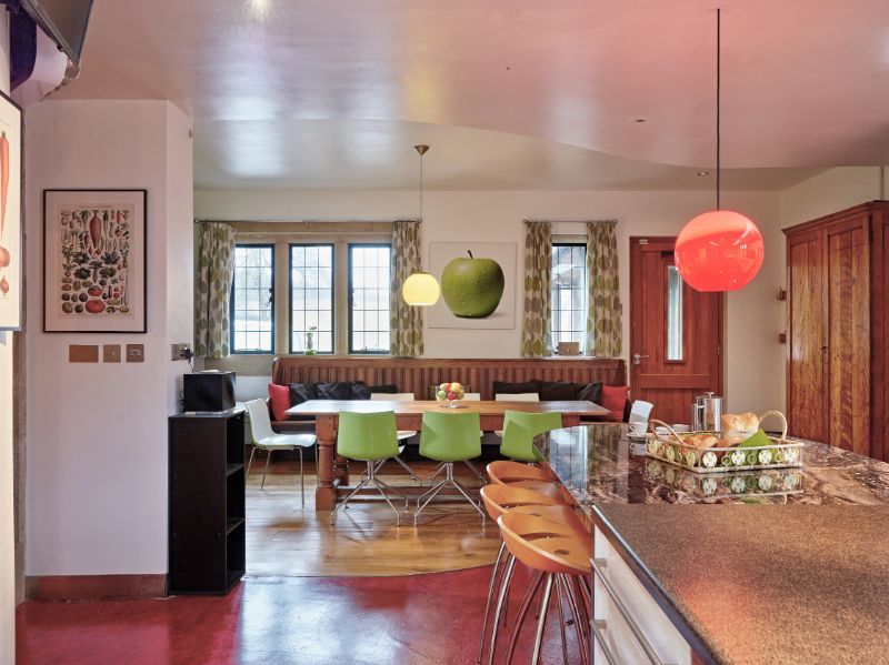 Bright dining room with wooden table, green chairs, red and green pendant lights, and large windows