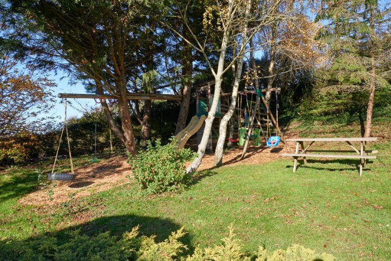 Backyard with a picnic table, swing set, trees, and a grassy lawn in sunlight