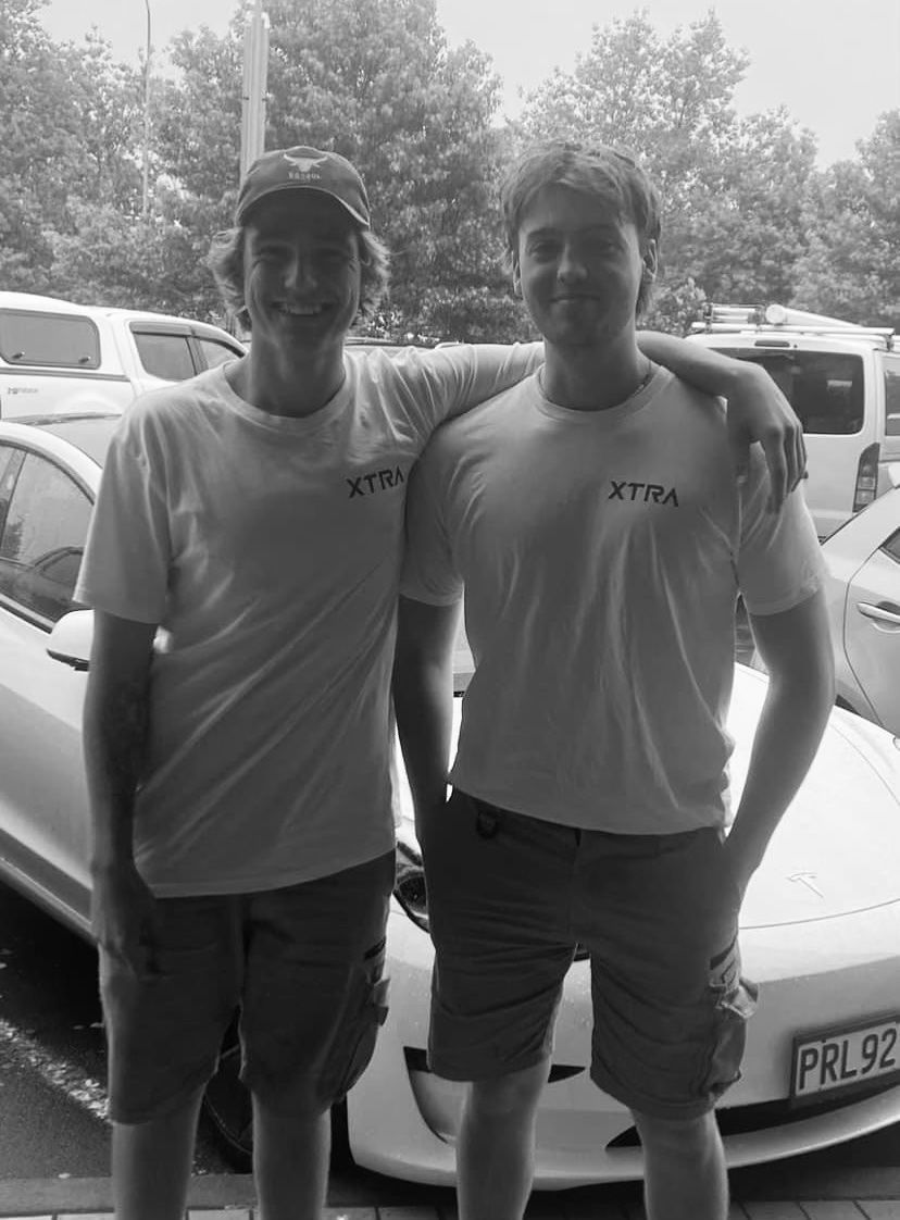 Two men are posing for a picture in front of a car.