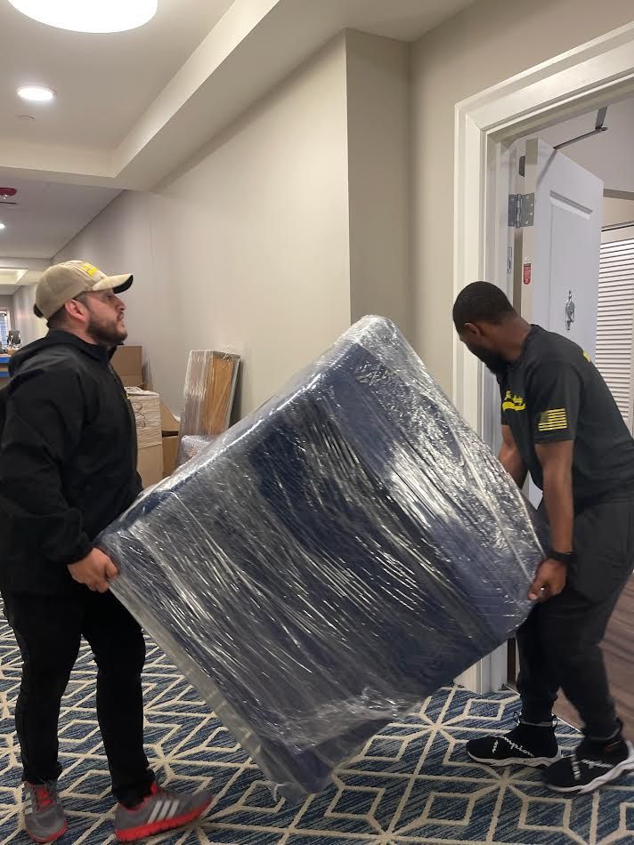 Two people carrying a large, plastic-wrapped, blue object through a hallway doorway.