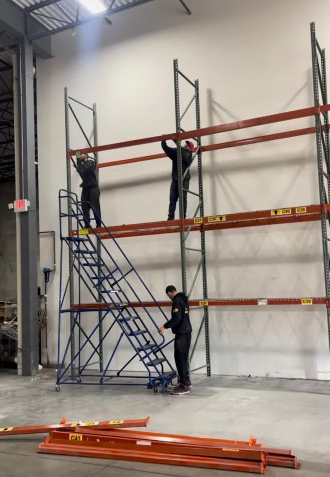 Three workers installing orange shelves on a metal storage rack in a warehouse.