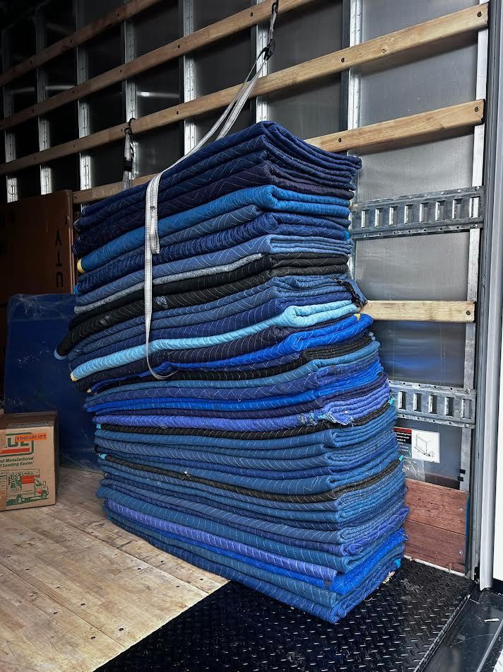 Stack of blue moving blankets inside a truck, secured by a strap hanging from above.