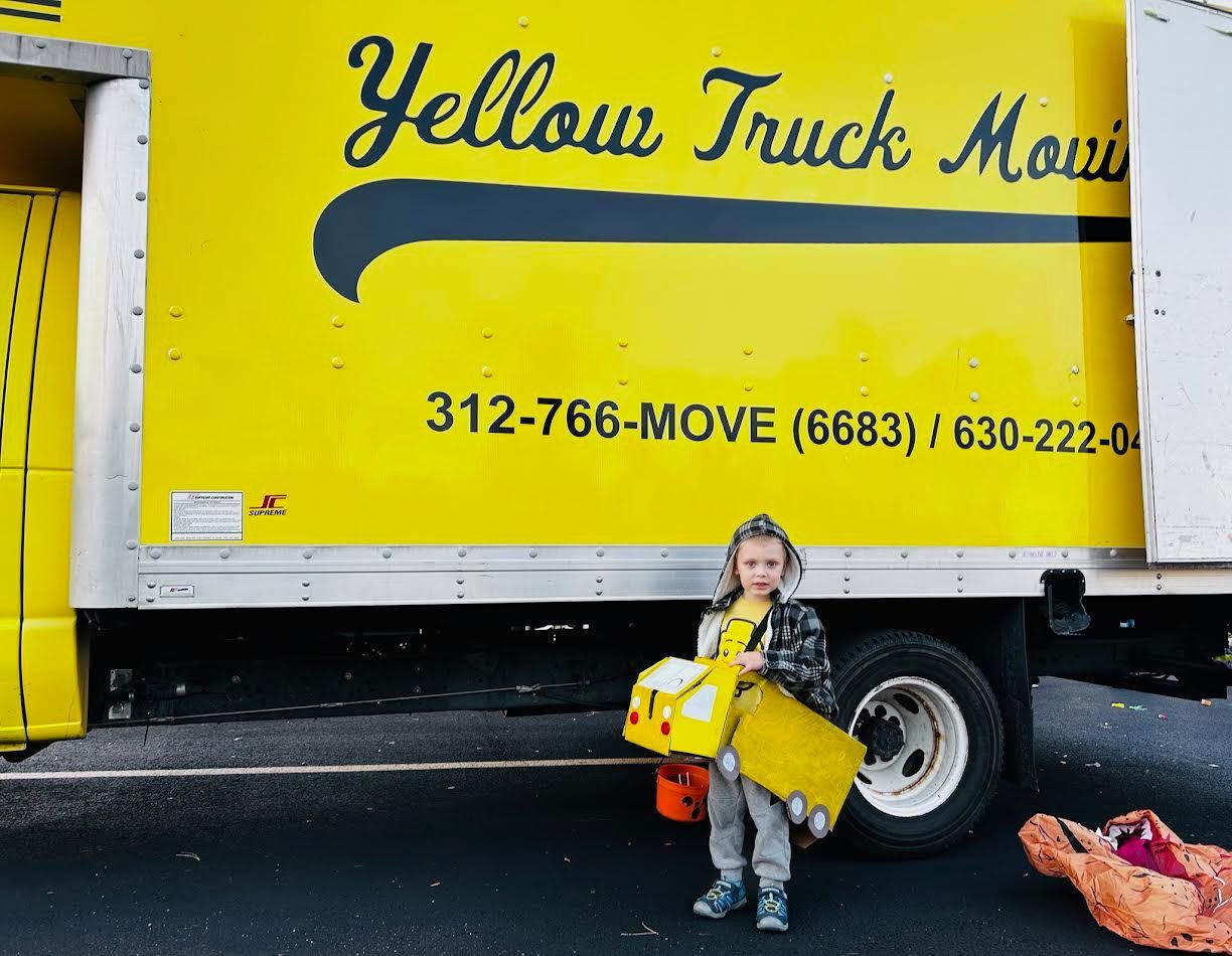 Child holding toys stands in front of a yellow 
