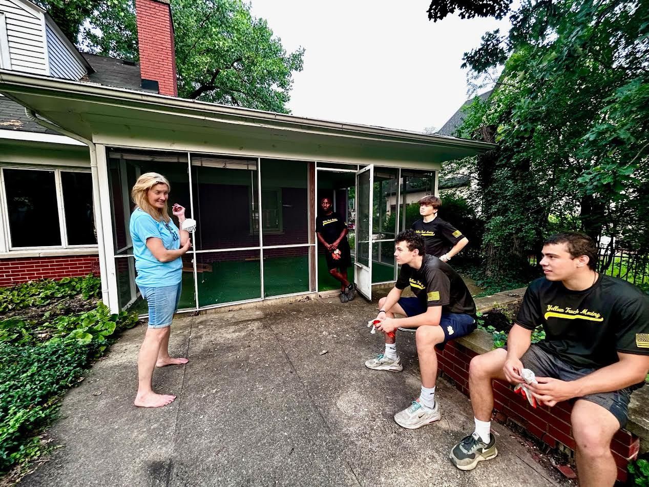 Woman talking to four people on a patio. Group in front of a screened porch, near a house.