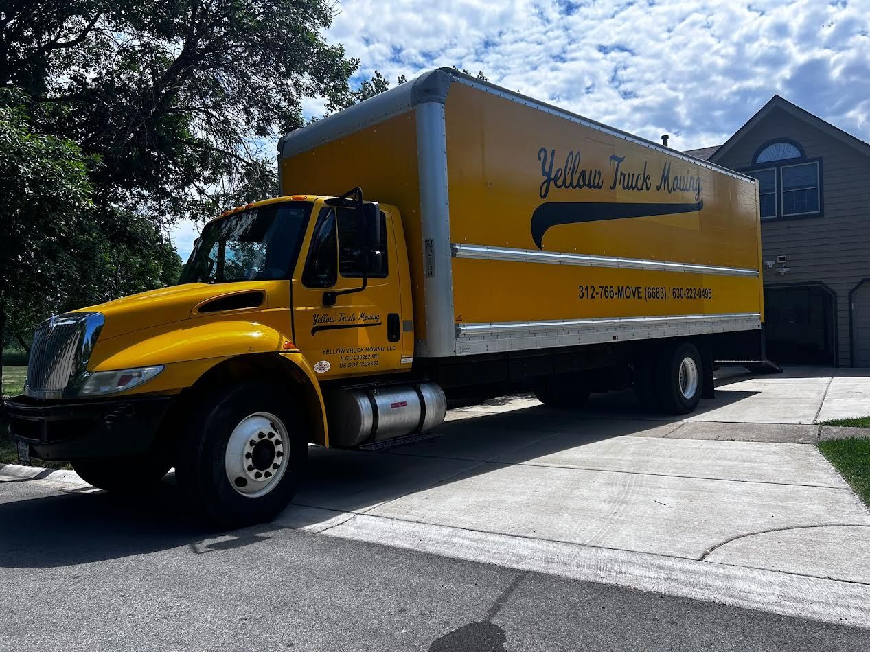Yellow moving truck parked in a driveway. Building in the background.