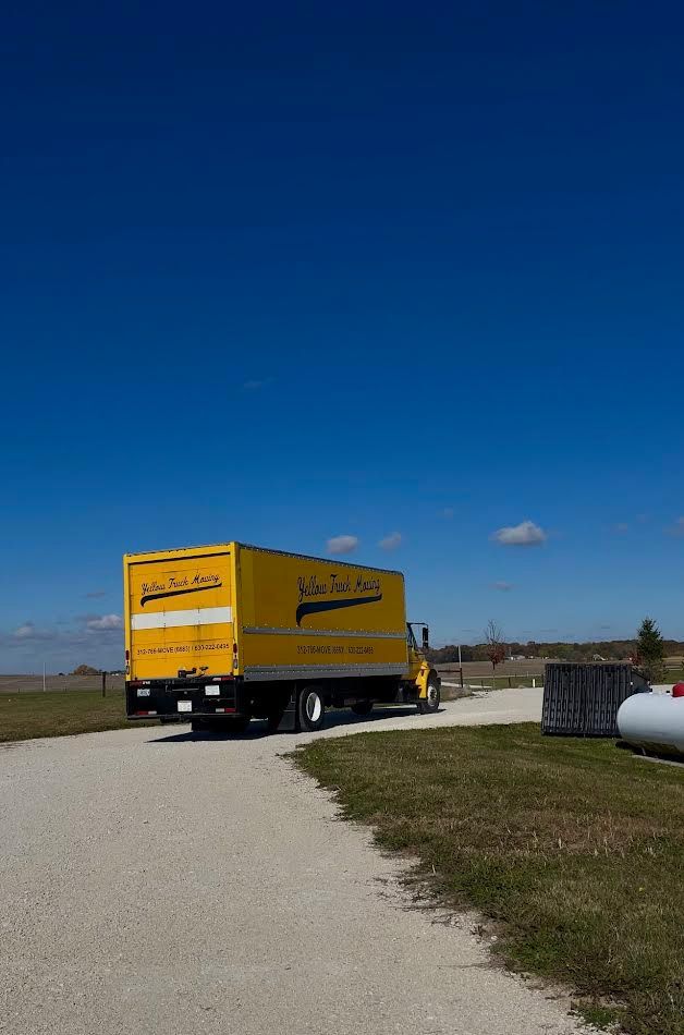 Yellow delivery truck on a gravel road against a blue sky.