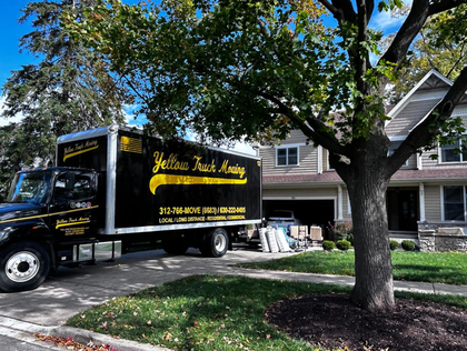 Yellow Truck moving truck parked in front of a house on a sunny day.