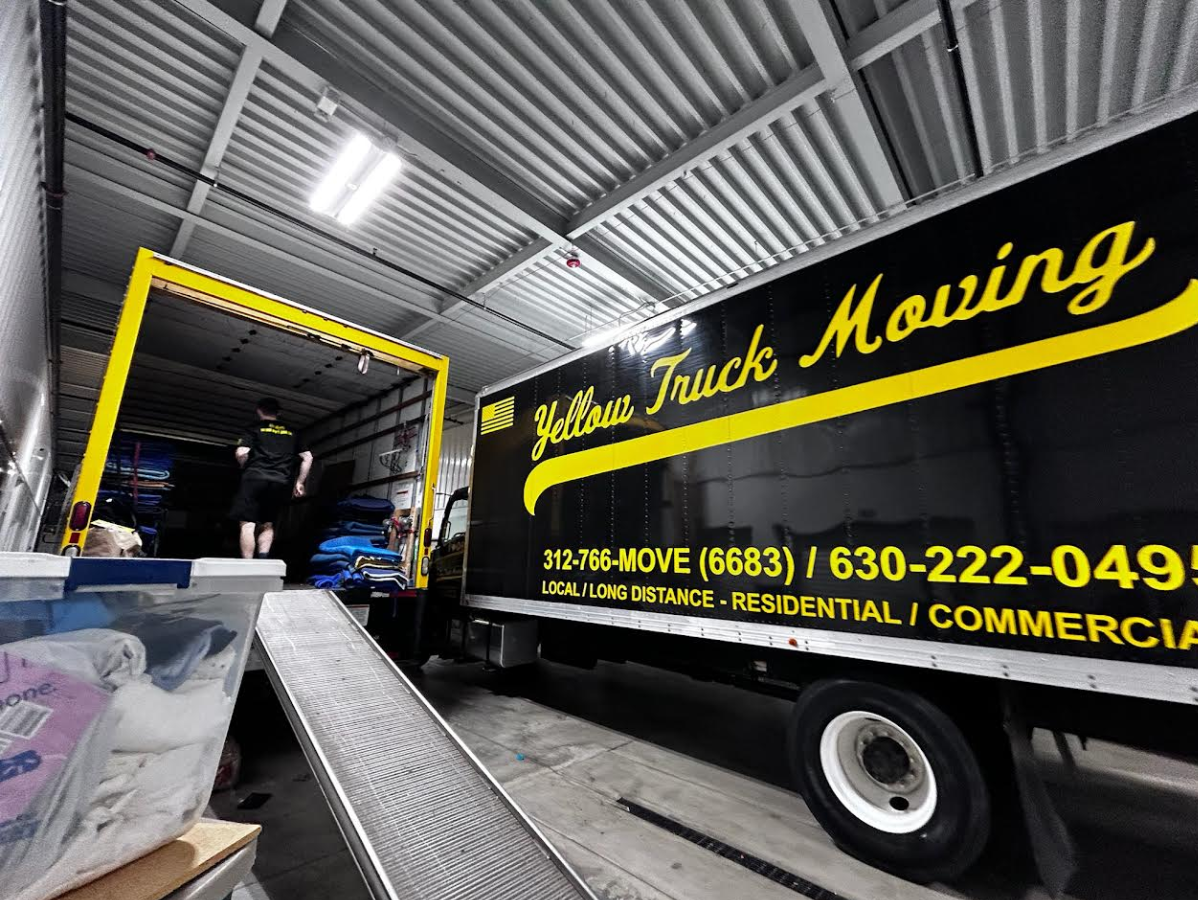 Yellow Truck Moving truck inside a loading dock. Black truck with yellow logo; ramp leading into the truck.