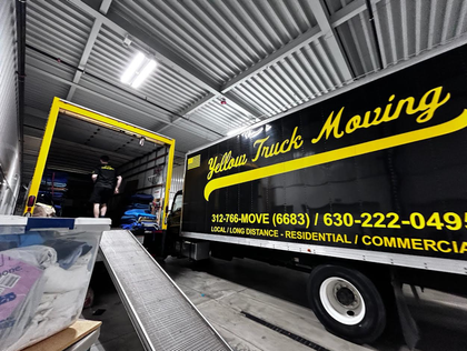 Yellow moving truck loading goods inside a garage.