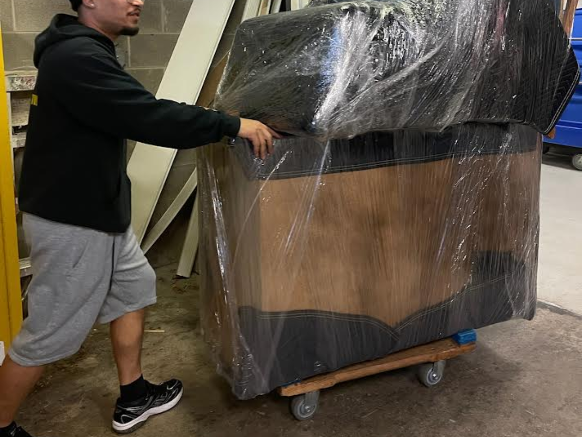 Man pushing a large wrapped box on a dolly.