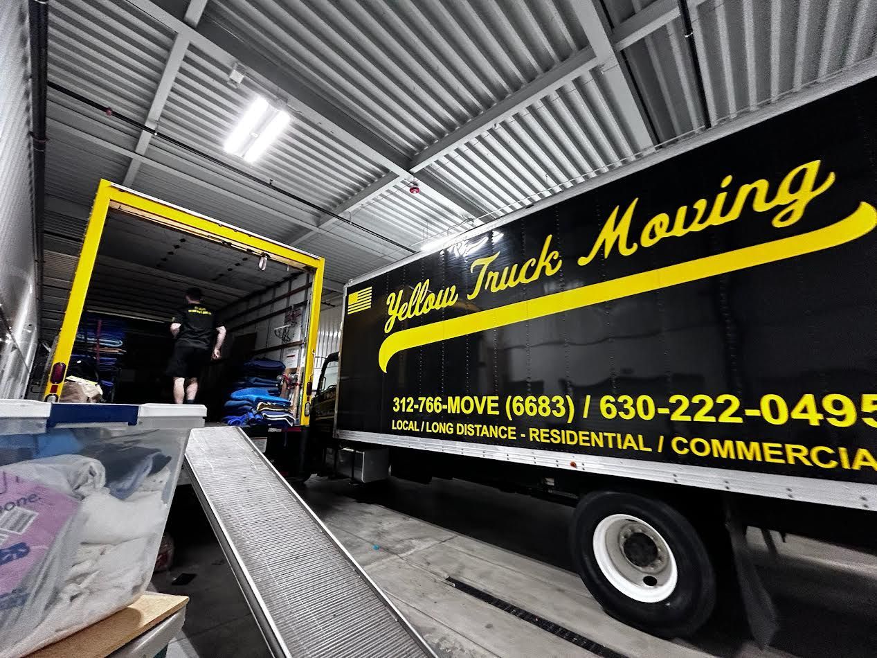 Yellow Truck Moving truck parked with a ramp and a yellow frame, in an indoor warehouse, worker loading items.