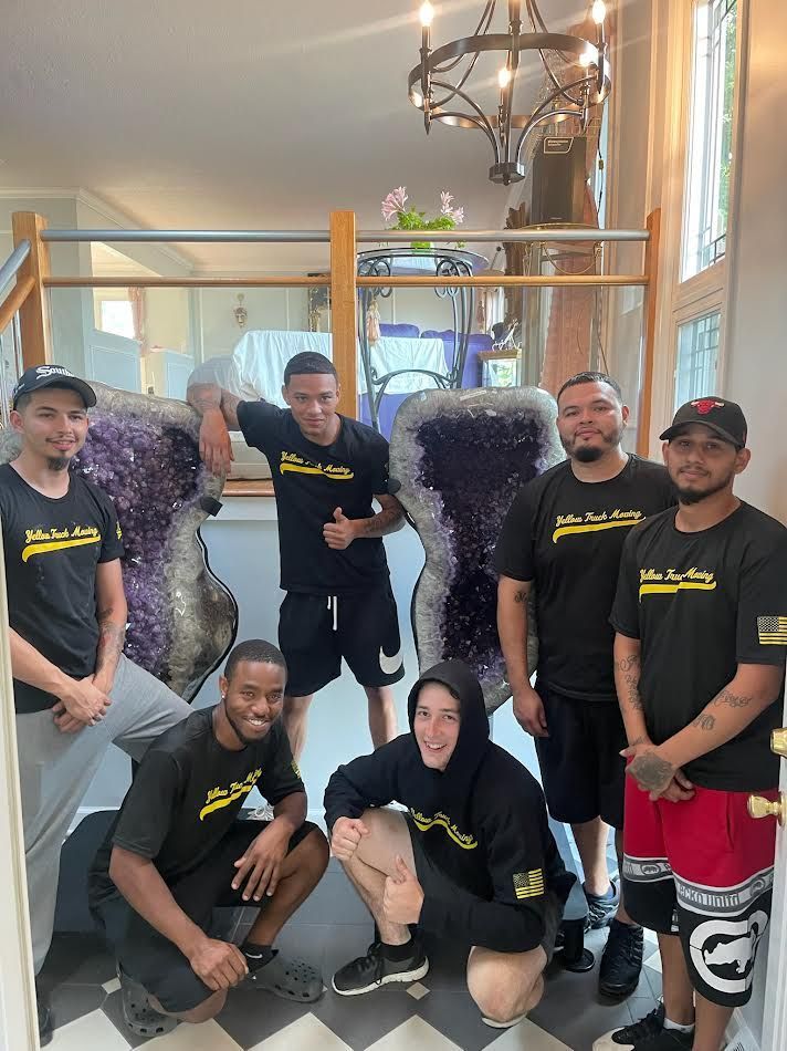 Group of men posing by large amethyst crystals inside a building; men wearing black shirts with logo.