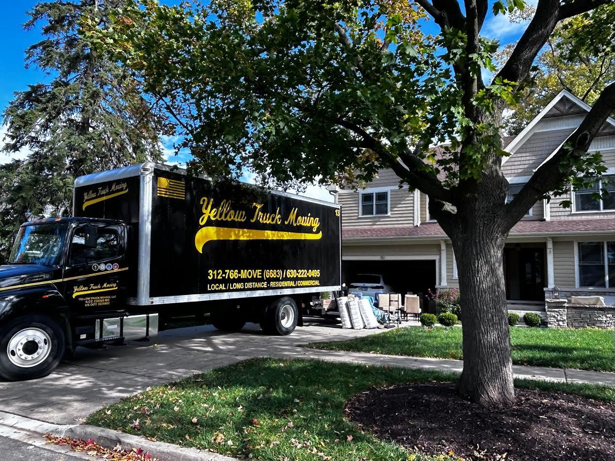 Moving truck parked in front of a house, furniture visible. Yellow truck says 