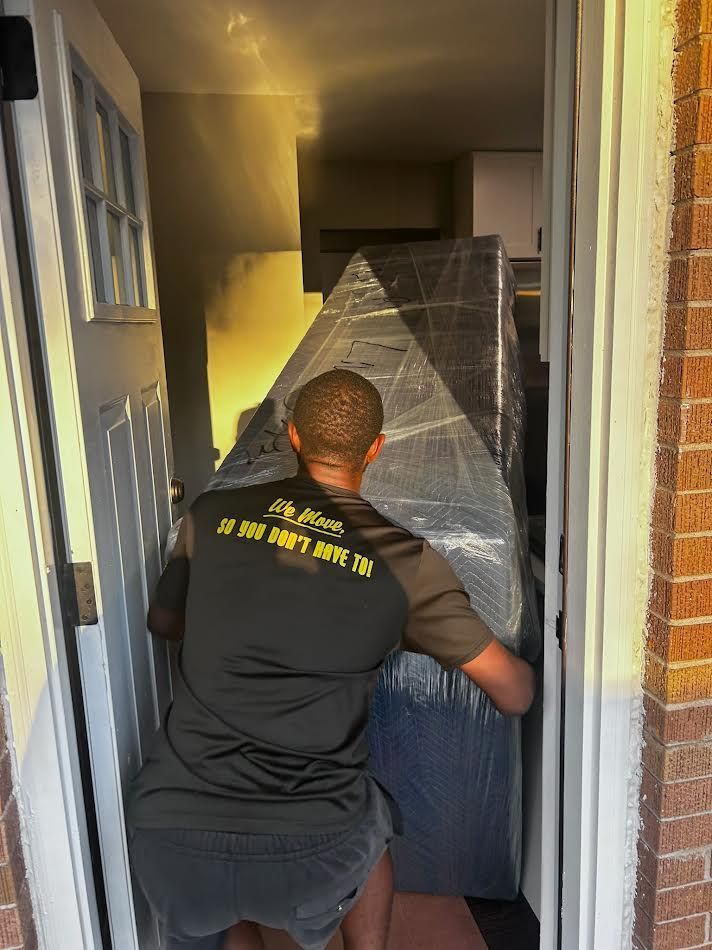 A person carrying a wrapped piece of furniture through a doorway. The person is wearing a black shirt.