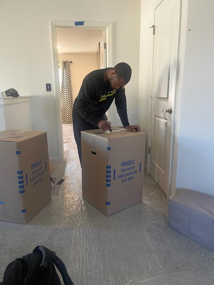 Person labeling a cardboard moving box in a room with two other boxes.