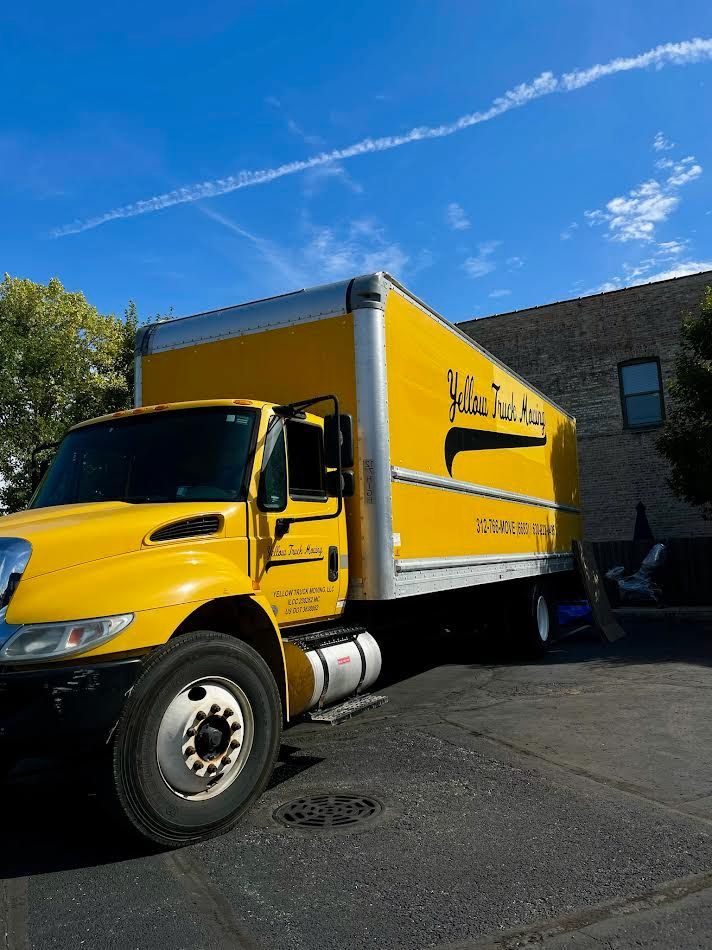 Yellow moving truck parked near a building on a sunny day.