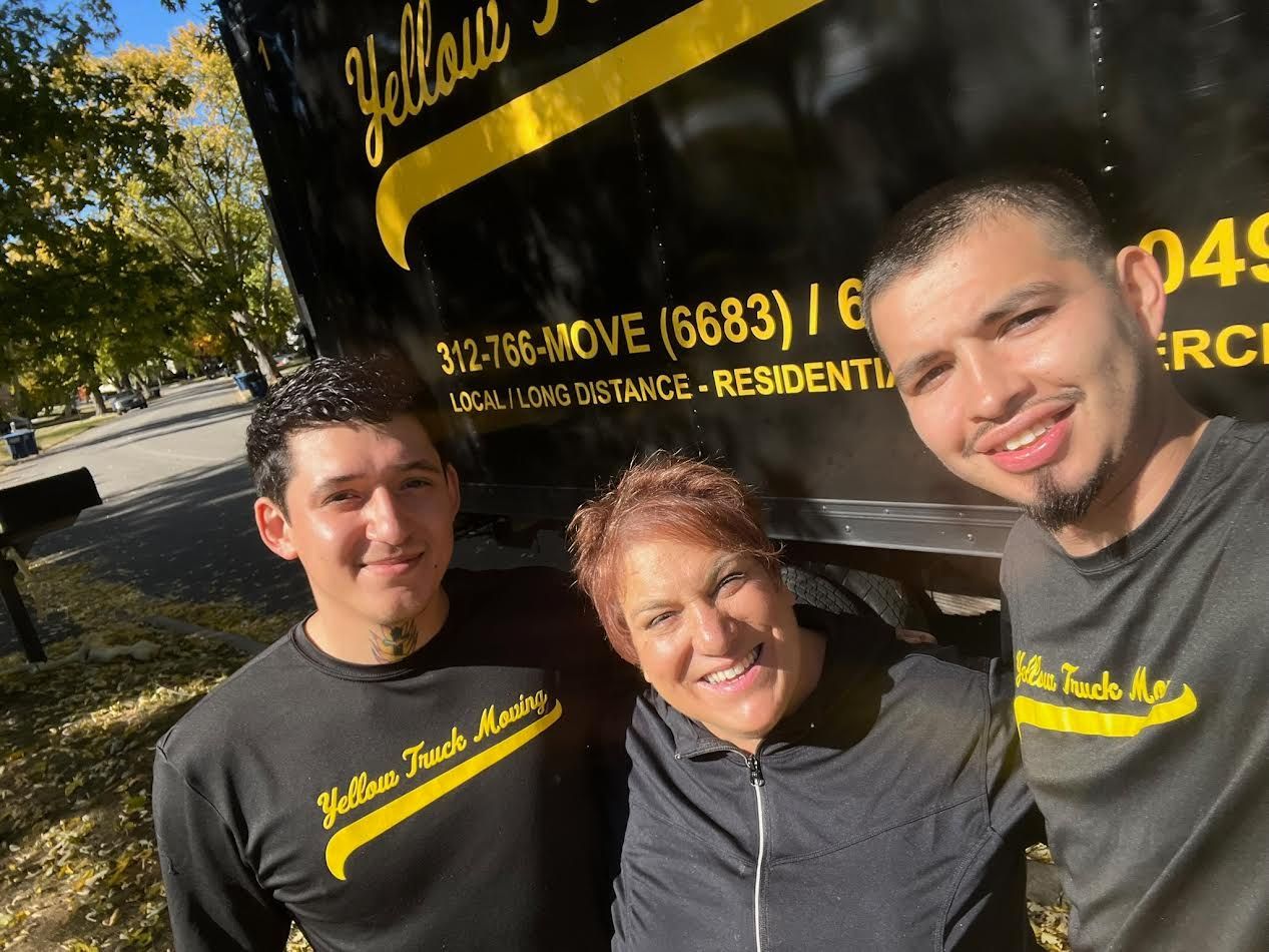 Three people smiling in front of a yellow and black truck, logo says 