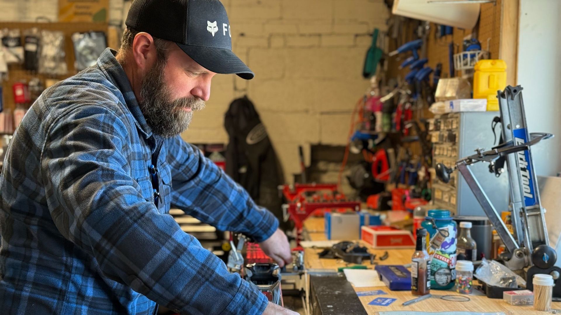 A man in a plaid shirt is working on skis in a garage.