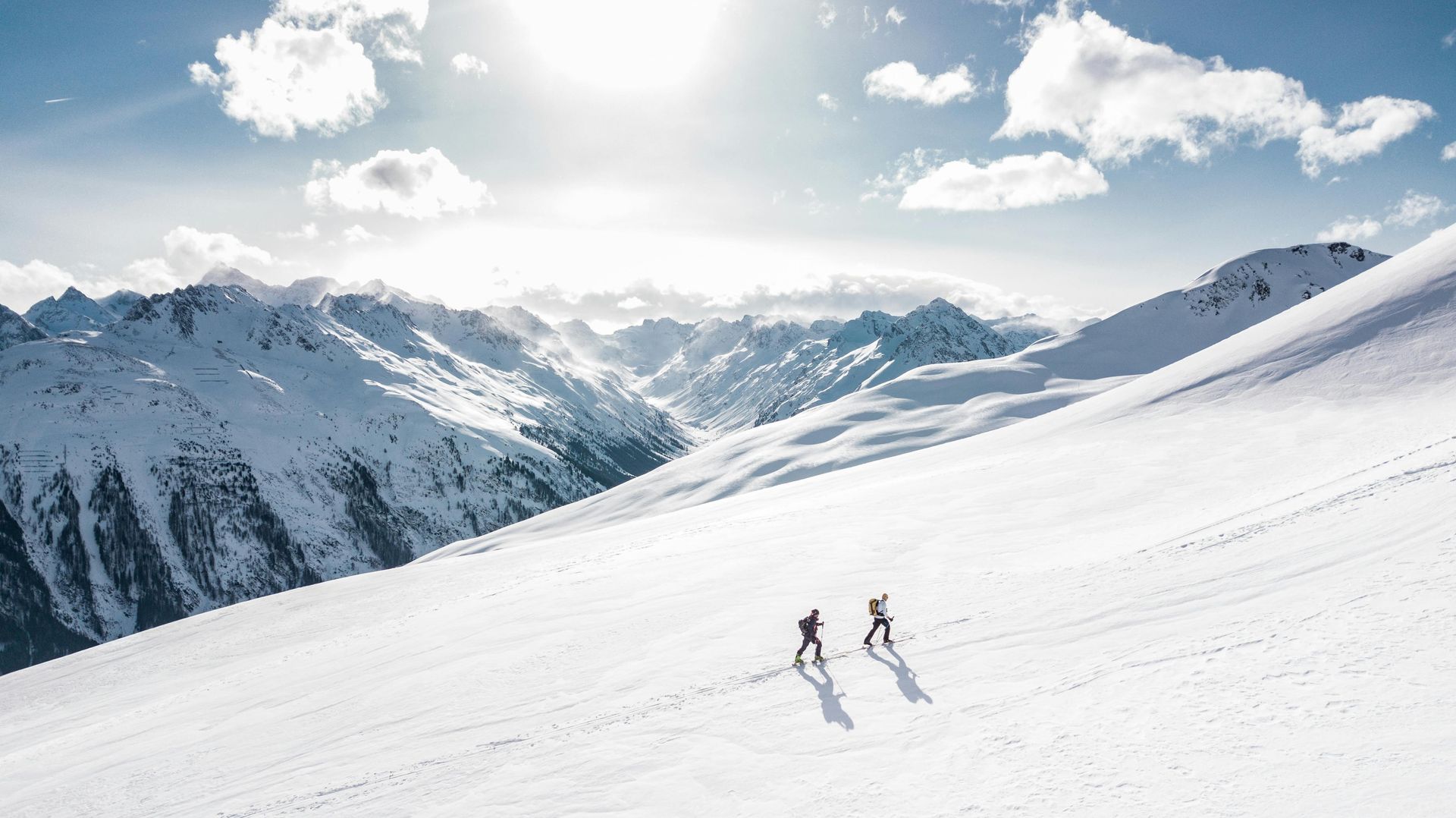 Two people are skiing down a snow covered mountain.