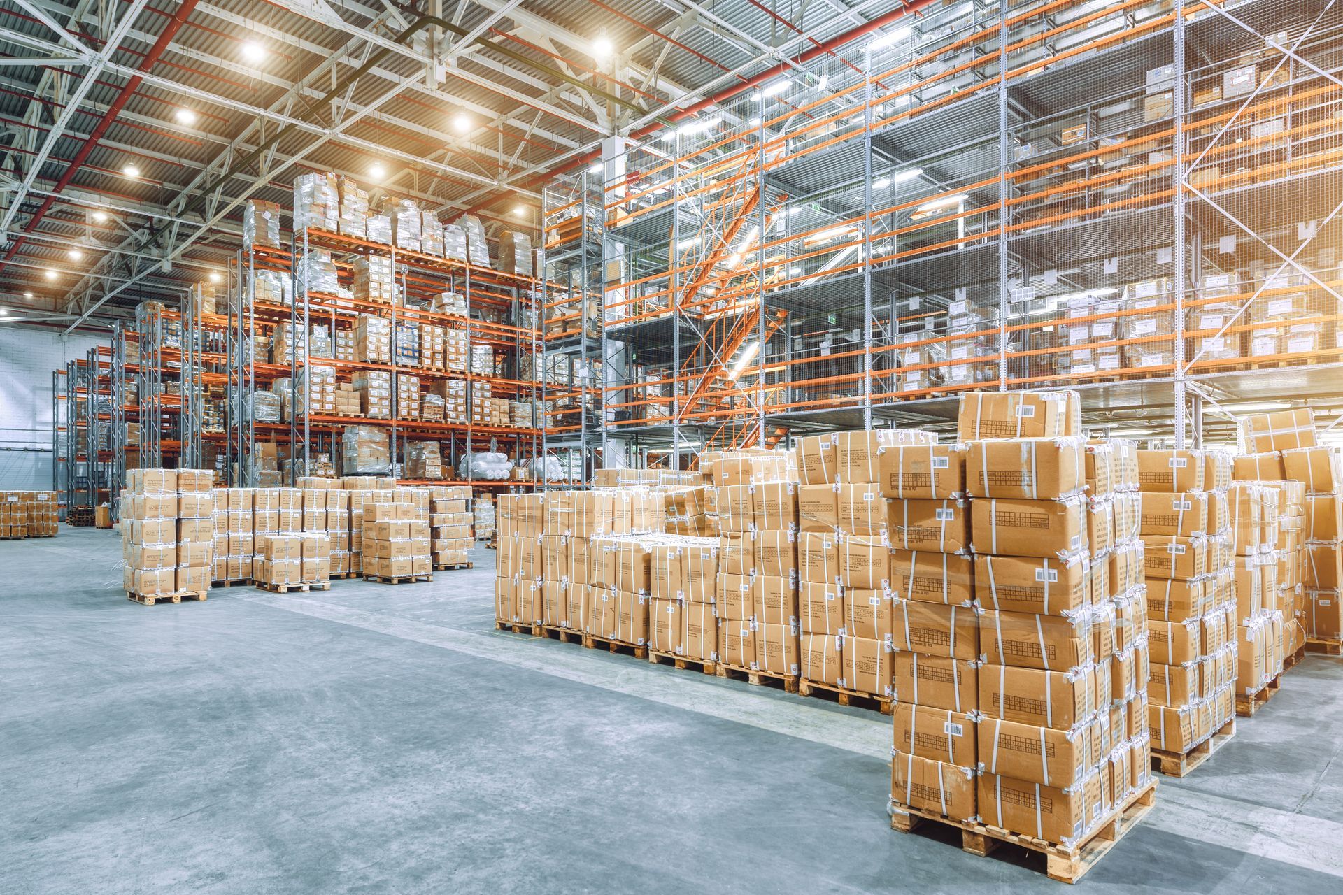 Spacious warehouse with stacked boxes on pallets and tall shelving units for organized storage.