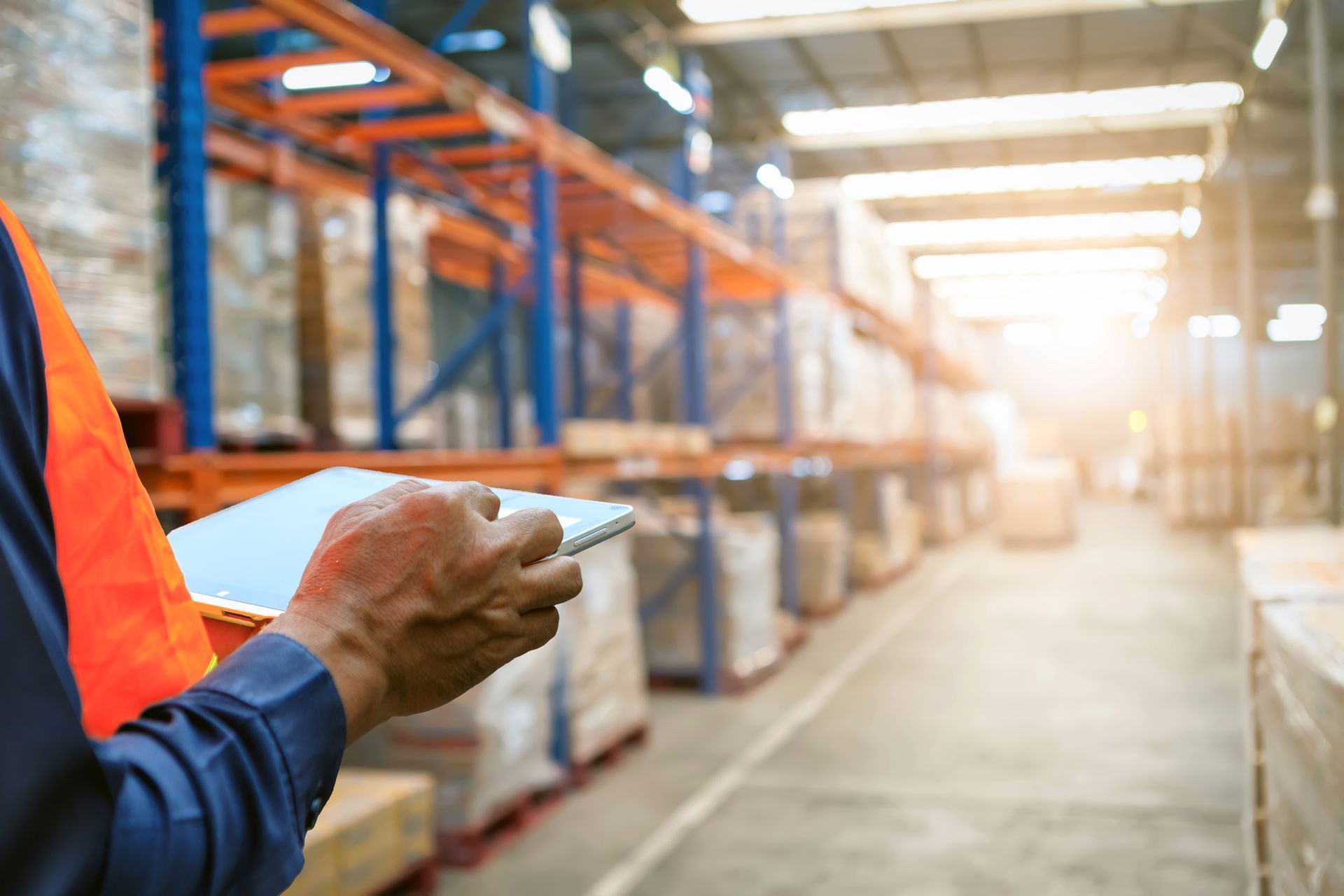 Worker using a tablet to manage inventory while standing in a large warehouse aisle.