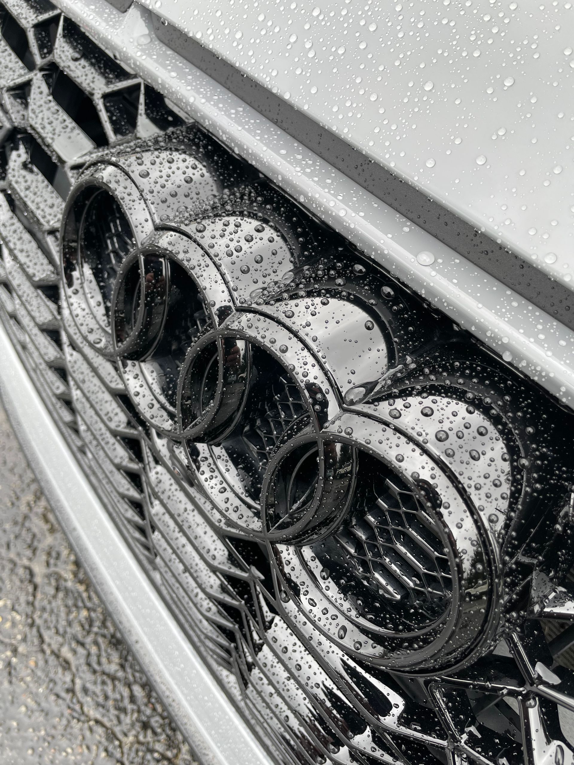 A close up of an audi grille with water drops on it.