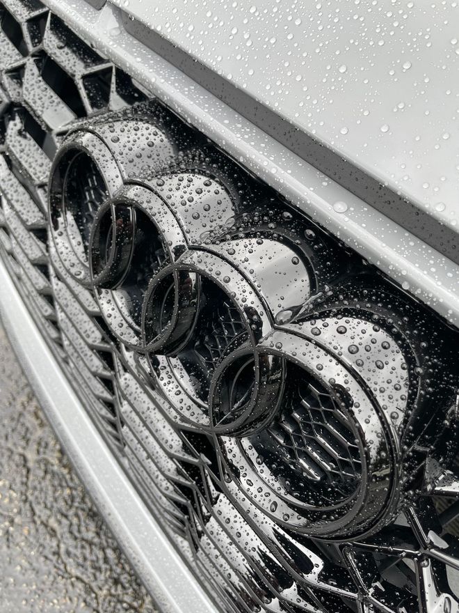 A close up of an audi grille with water drops on it.