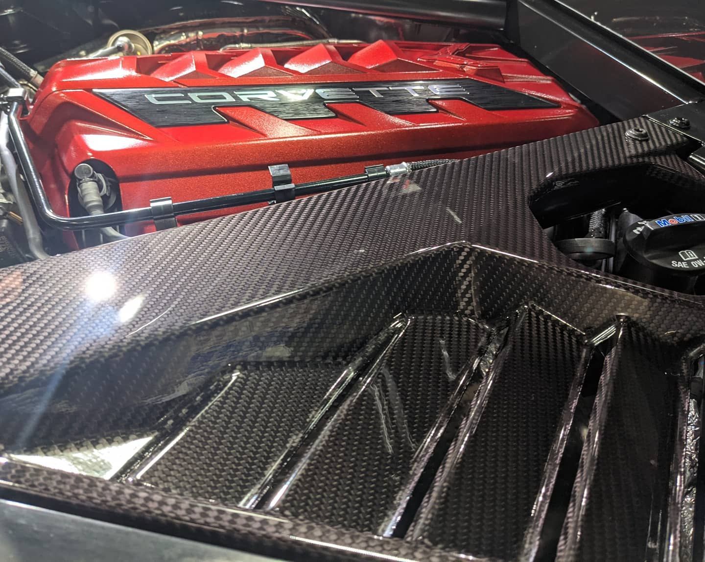 A red corvette engine is sitting under the hood of a car.