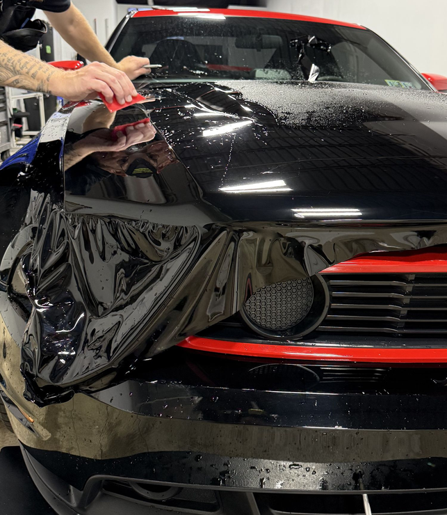 A man is cleaning the wheel of a black car with a sponge.