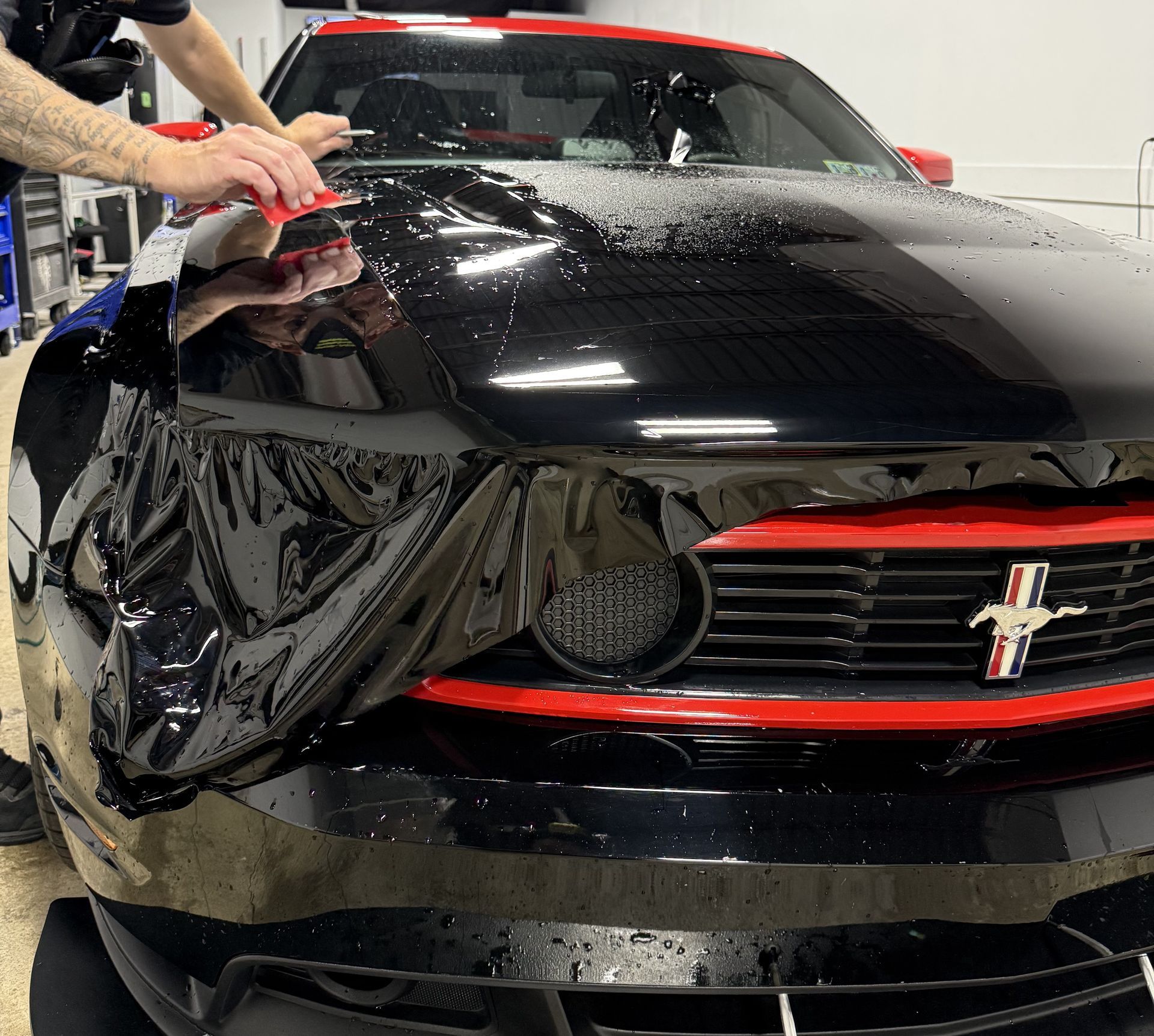 A man is cleaning the wheel of a black car with a sponge.