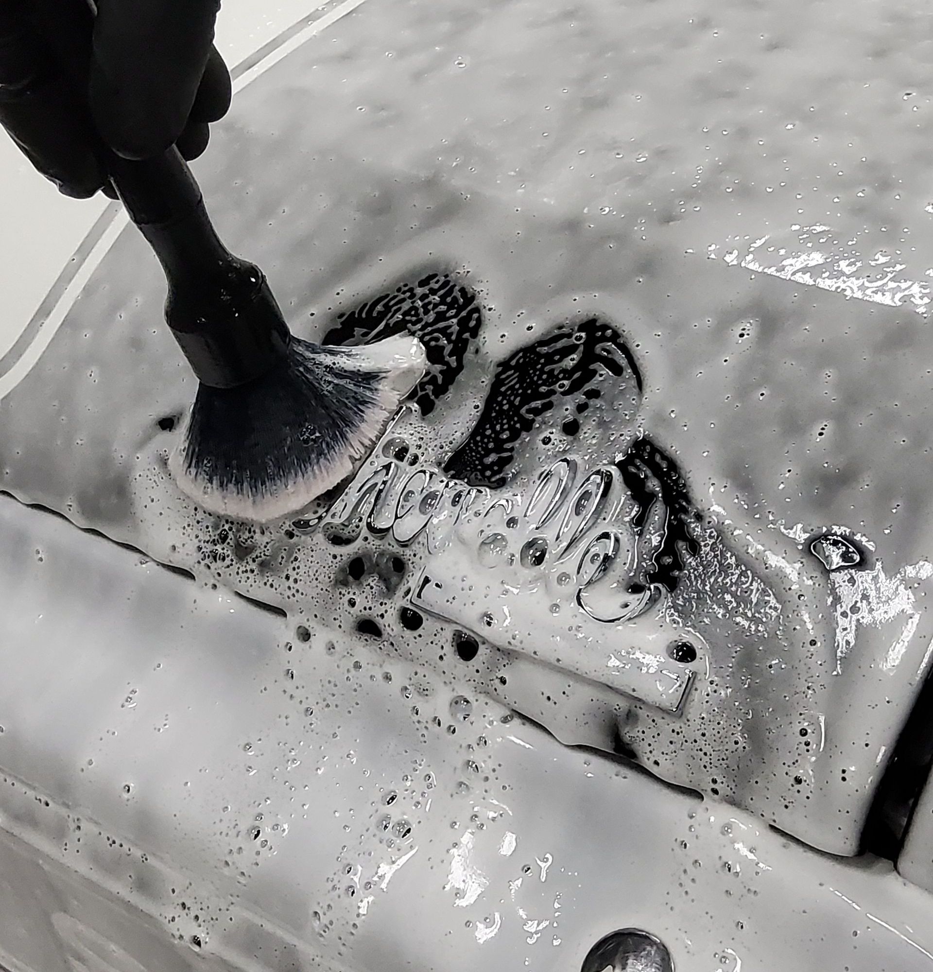 A person is cleaning a car with a brush and foam.