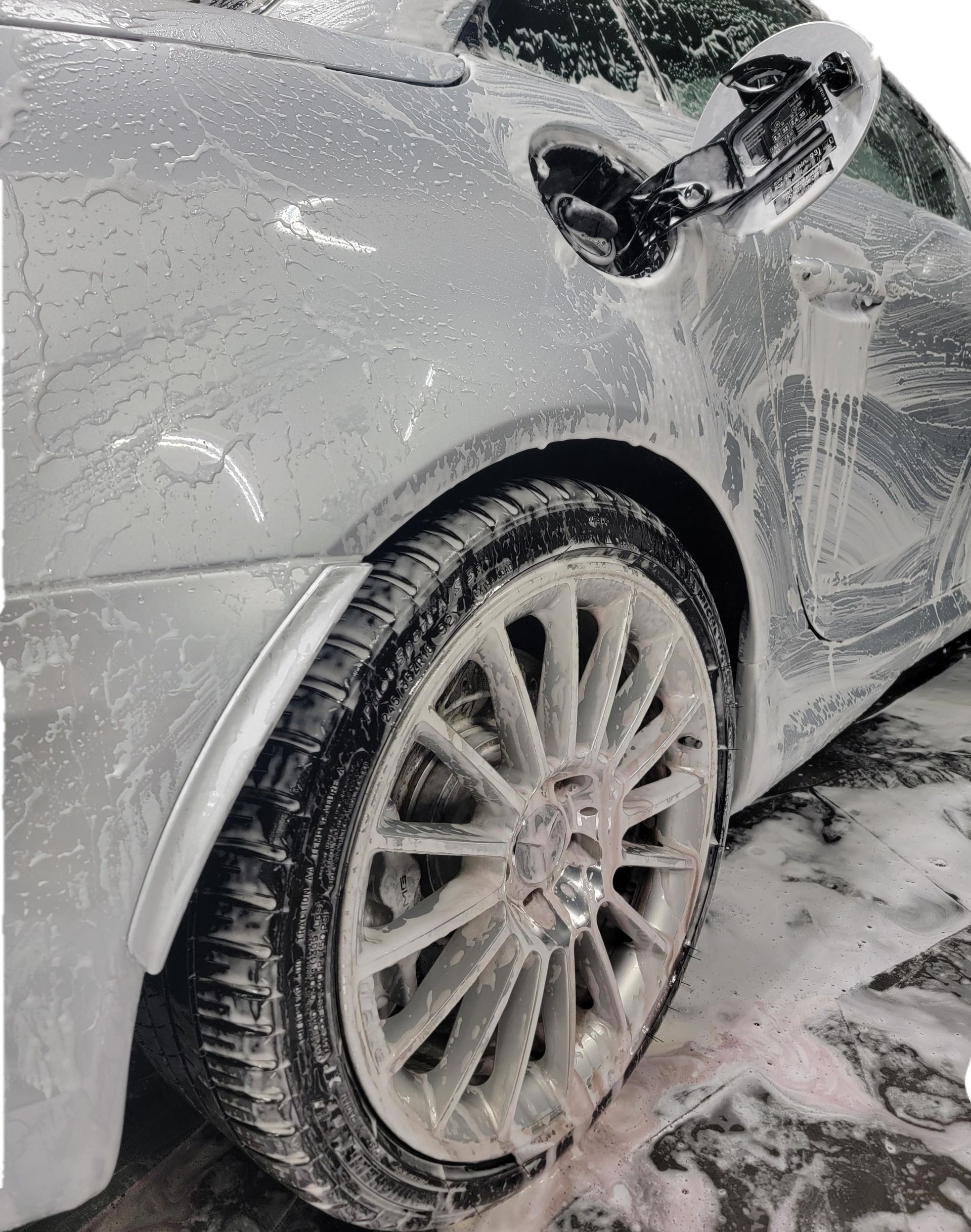 A man is cleaning the wheel of a black car with a sponge.
