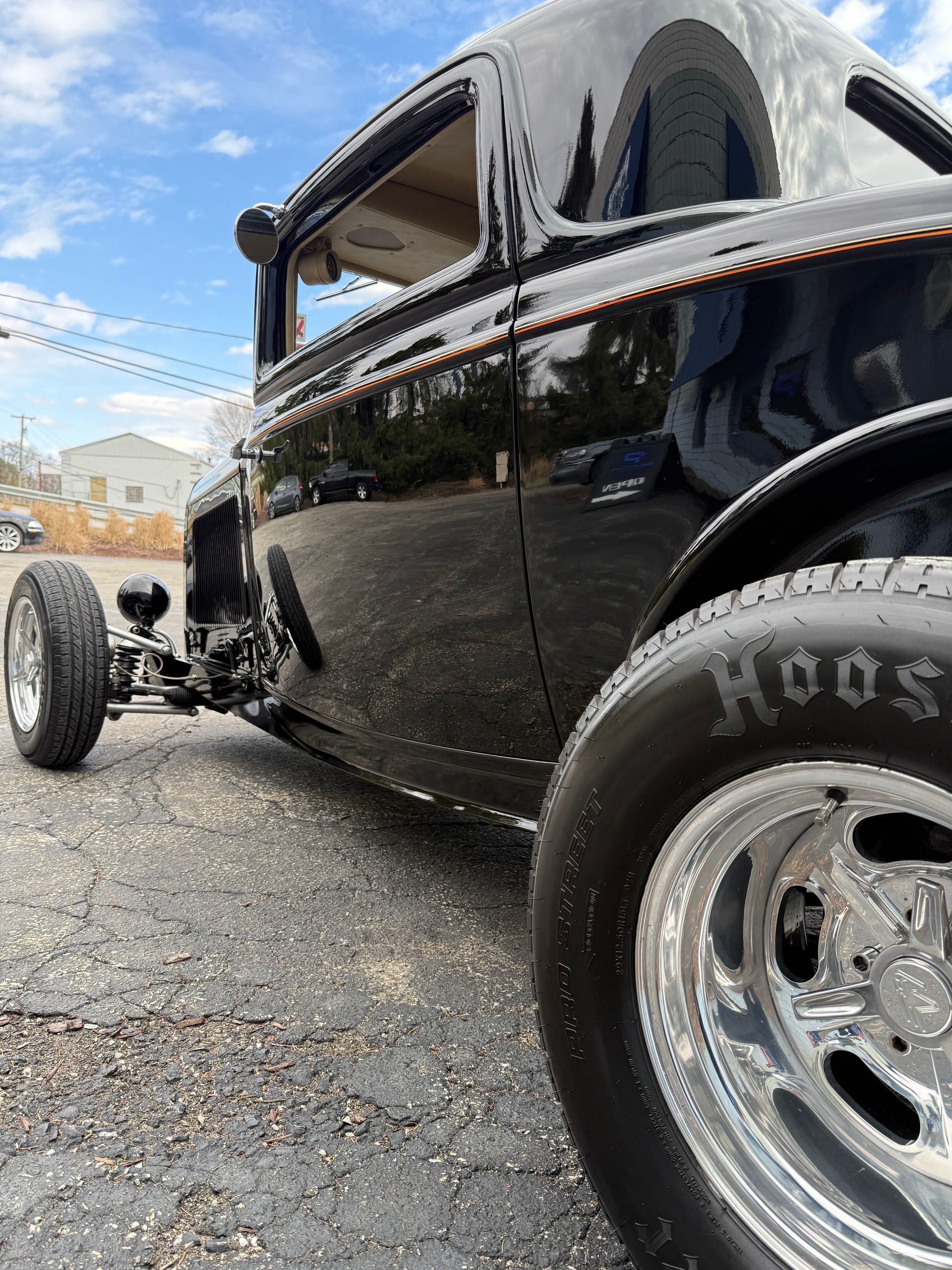 Black vintage hot rod with chrome wheels parked on gravel under a blue sky