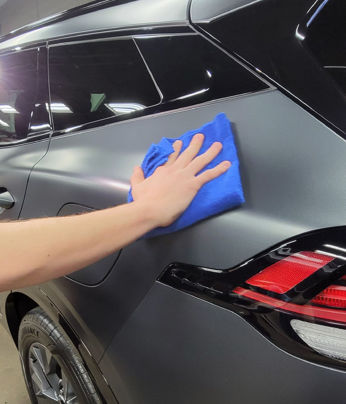 A man is cleaning the wheel of a black car with a sponge.