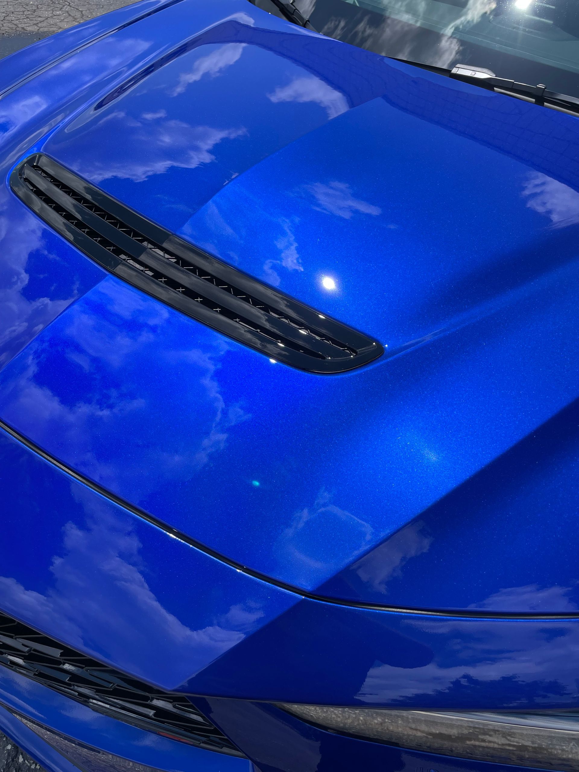 A person is using a blue squeegee to remove plastic from the hood of a car