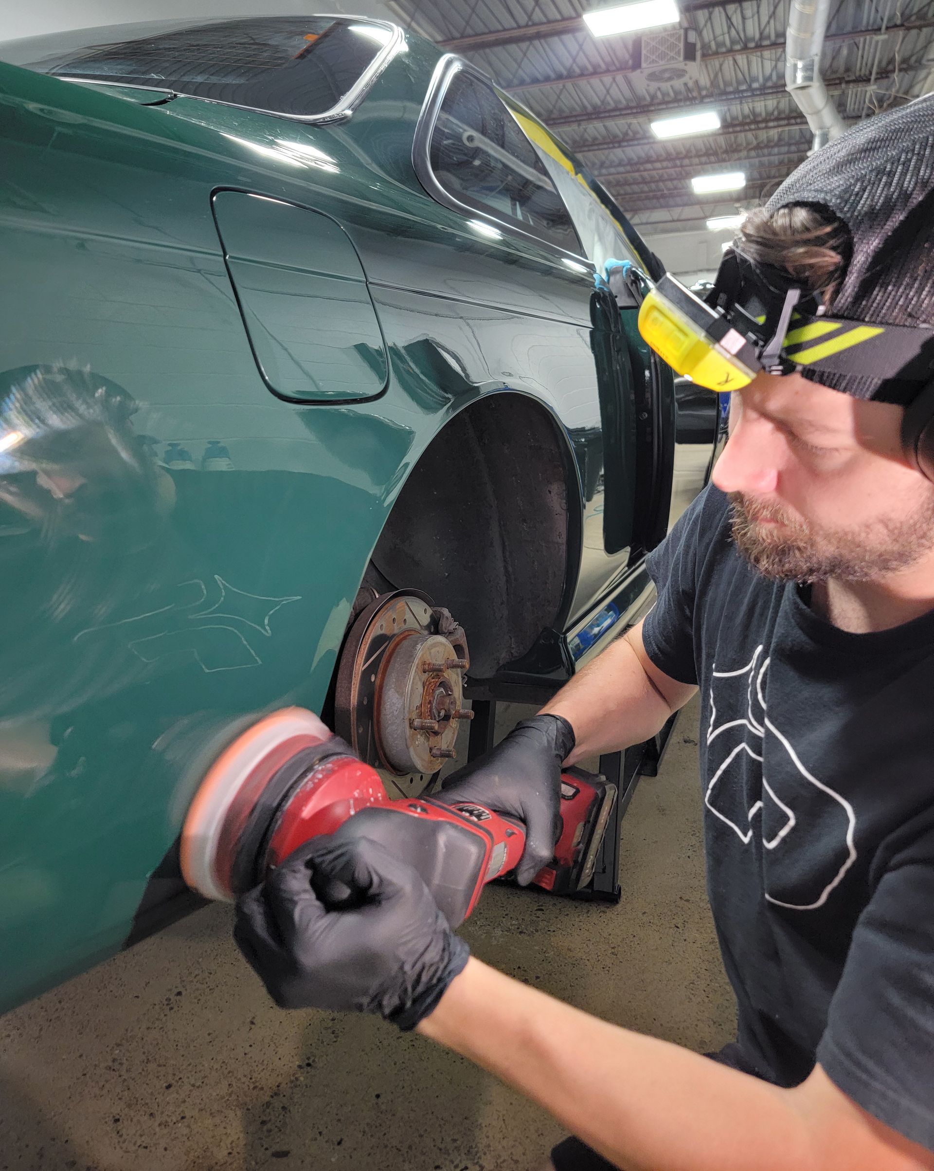A man is cleaning the wheel of a black car with a sponge.