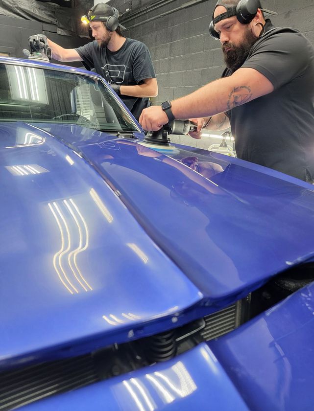 A man with a beard is polishing the back window of a car.