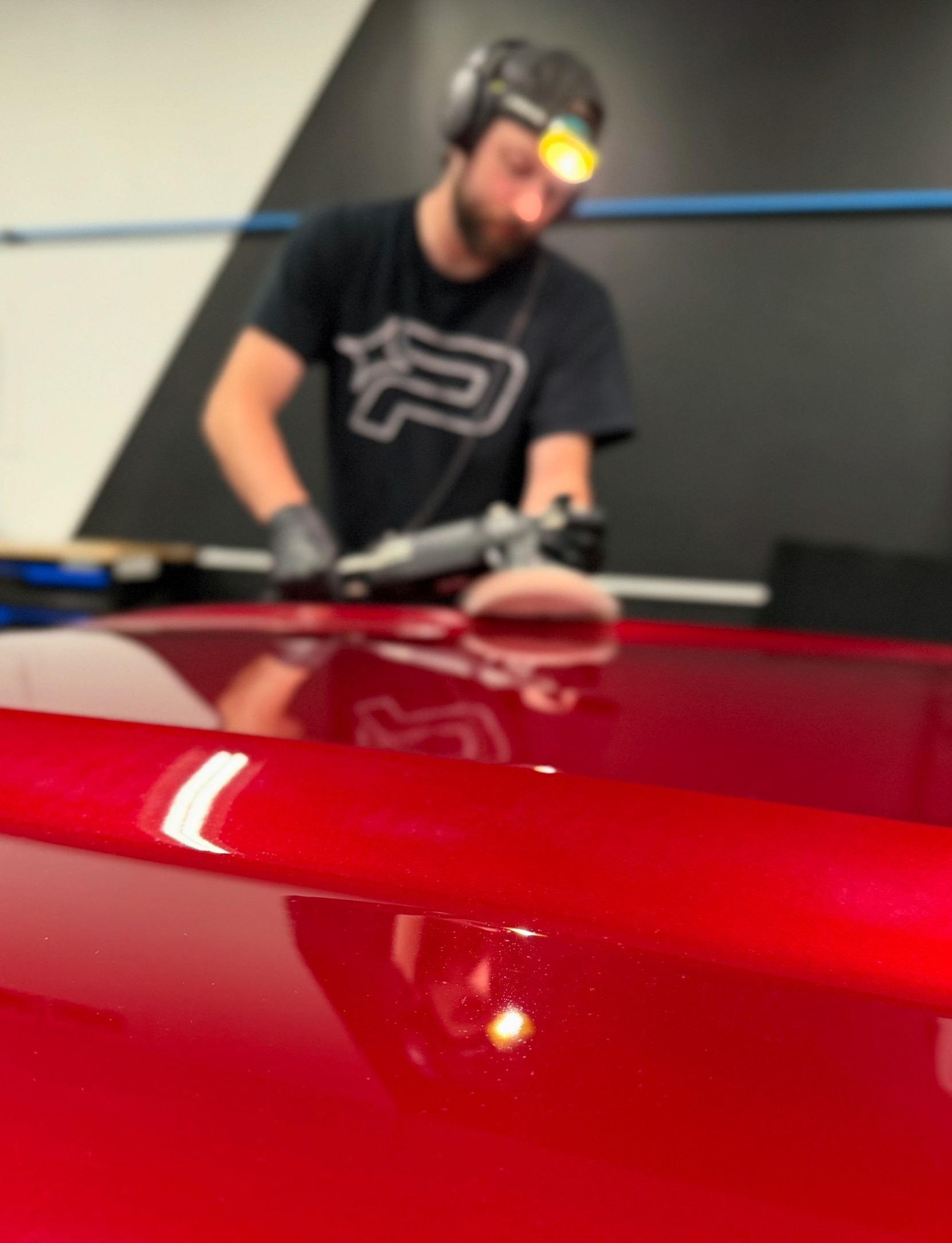 A person is using a blue squeegee to remove plastic from the hood of a car