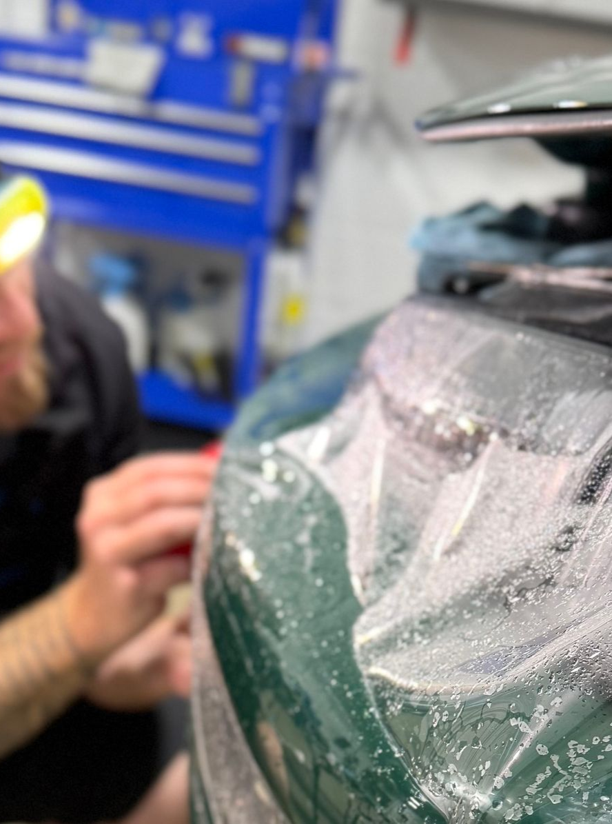 A man is cleaning the wheel of a black car with a sponge.