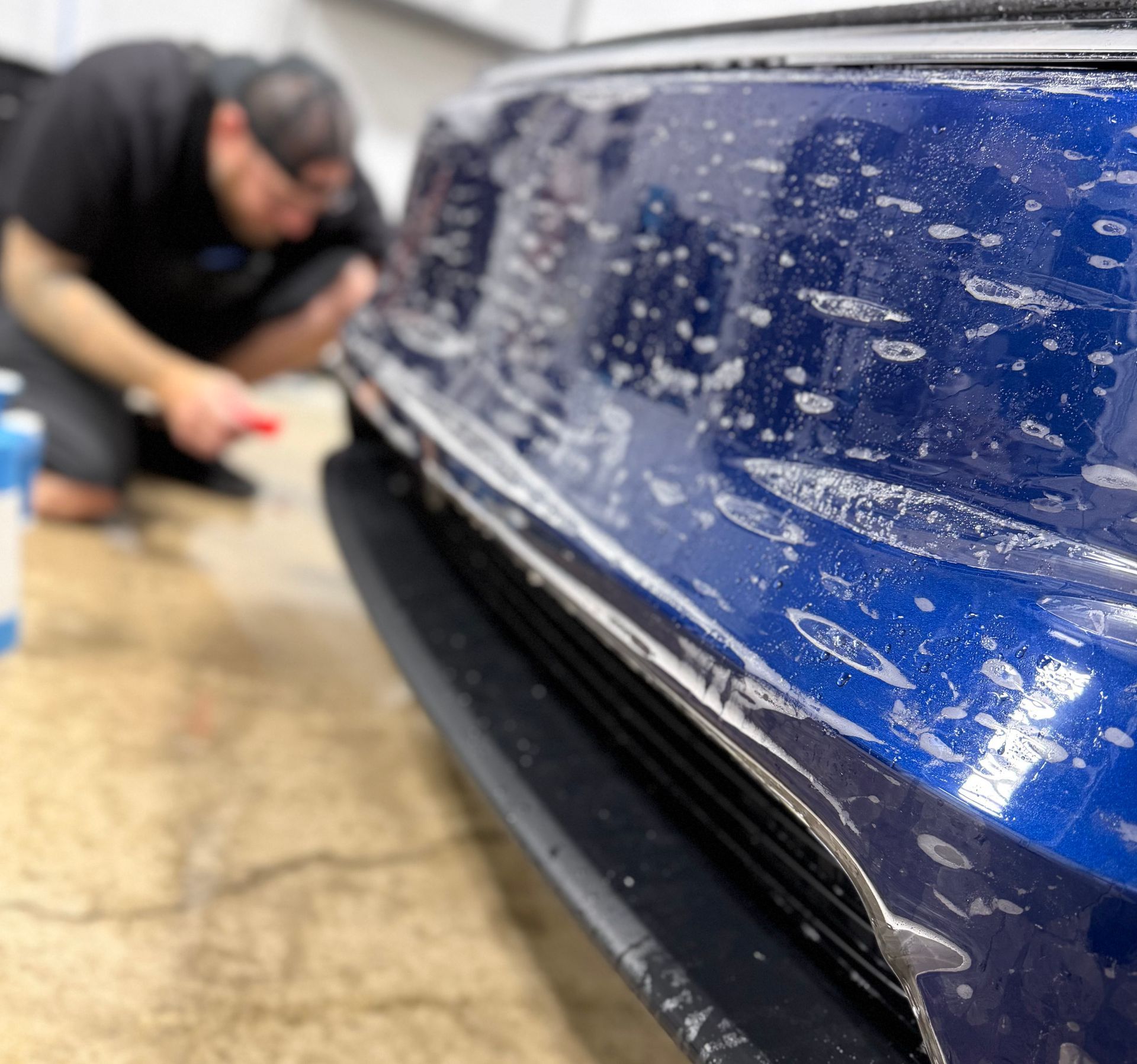 A person wearing black gloves is cleaning a red car with a sponge.