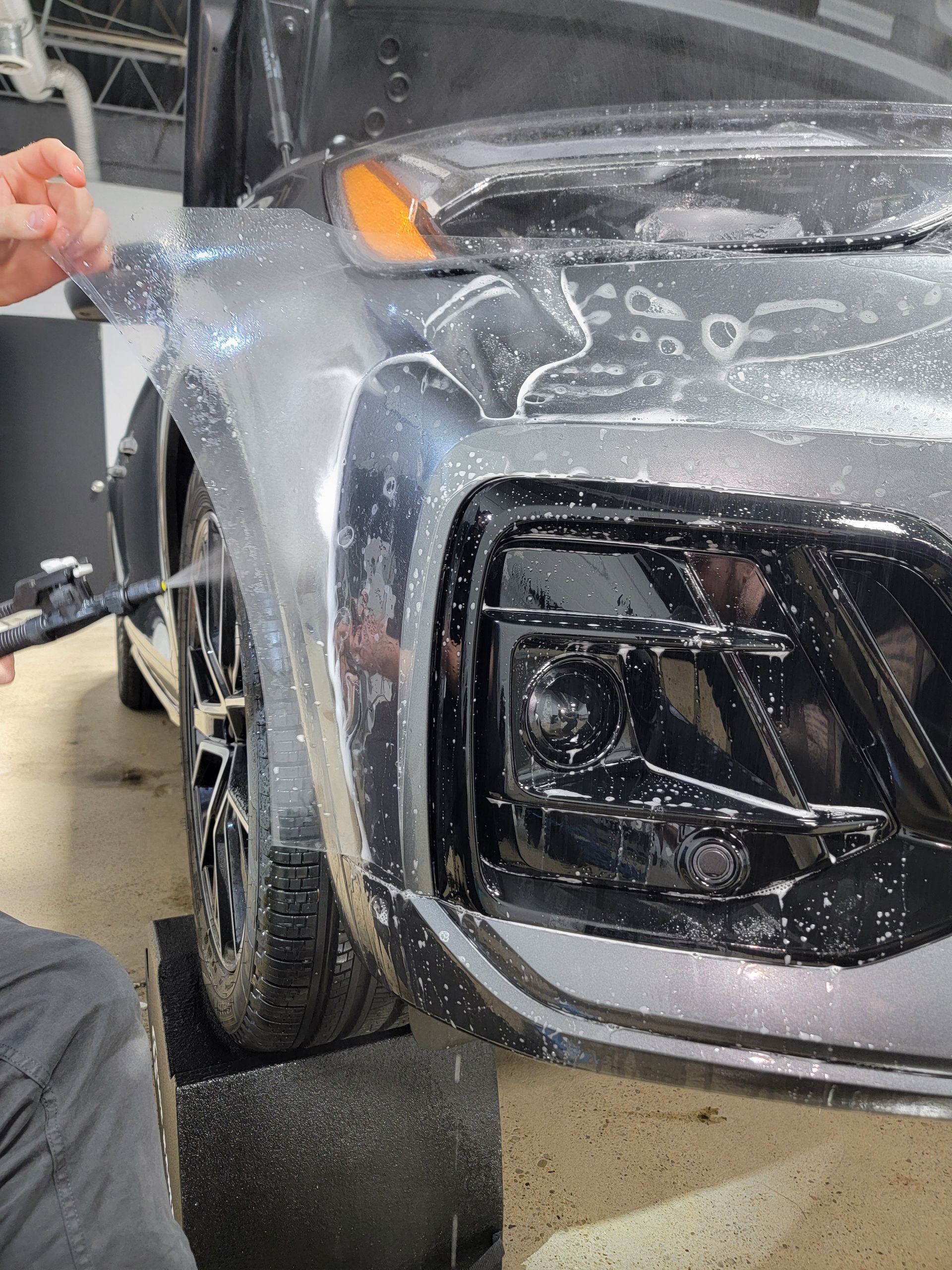 A man is cleaning the wheel of a black car with a sponge.