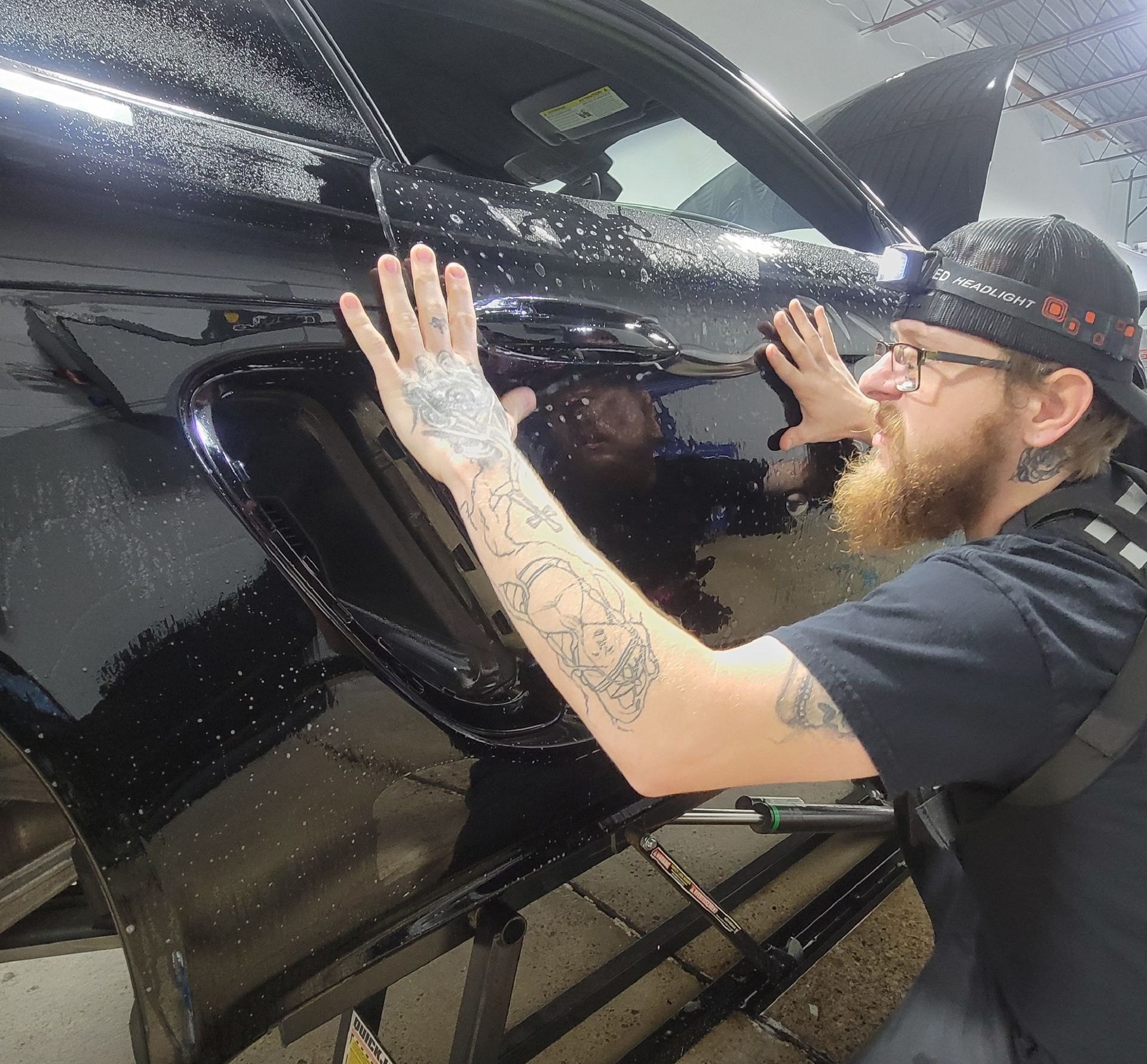 A person wearing black gloves is cleaning a red car with a sponge.