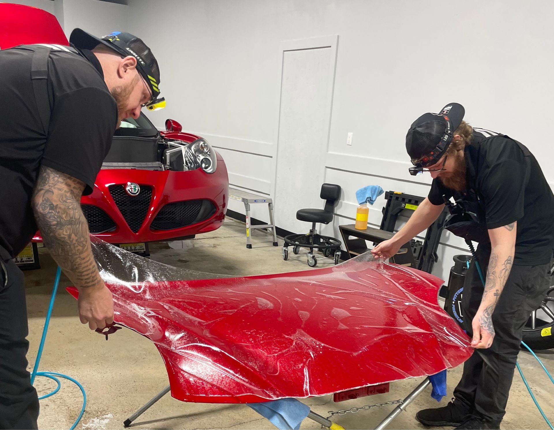 Two men are working on a red car in a garage.