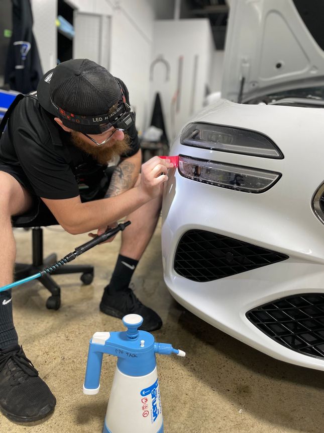 A man is cleaning the wheel of a black car with a sponge.